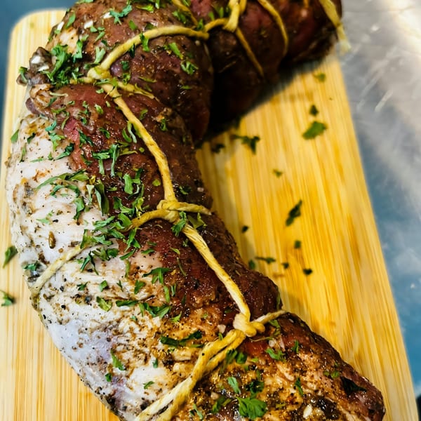 Two seasoned, tied meat roasts, one lighter and one darker, on a wooden cutting board.