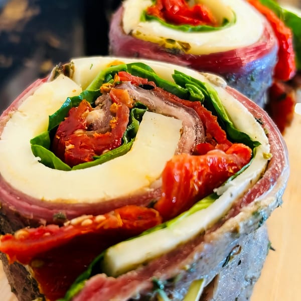 Close-up of a meat roll-up with cheese, sun-dried tomatoes, and greens, showcasing vibrant layers.