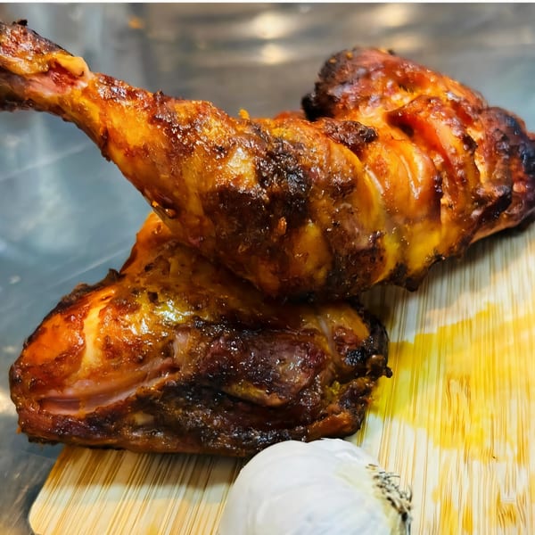 Two glistening, golden-brown BBQ chicken legs on a wooden board with a garlic bulb.