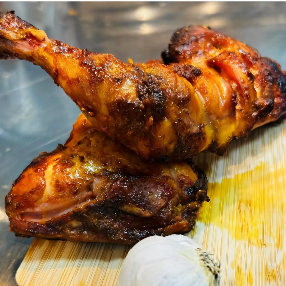 Two glistening, golden-brown BBQ chicken legs on a wooden board with a garlic bulb.
